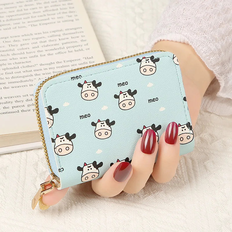 A showcasing of the Blue Cow and Cloud Meo Card Bag being held in a hand to show the size comparison. This print is some cute cows, little cows, and the word meo on top of a blue colored card bag. 