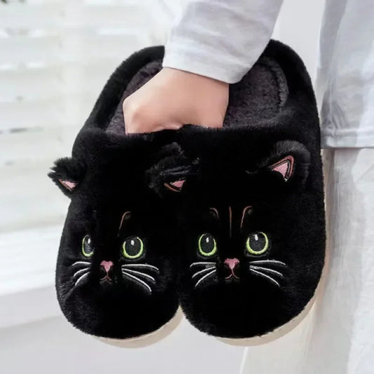 A showcase of the cute Fuzzy Black Cat Unisex House Slippers being held against a white background. 