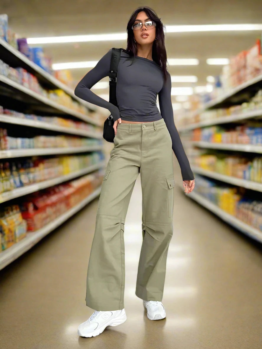 A woman wearing a grey slim fit long sleeve with khaki straight legged pants and white tennis shoes. She is standing in a grocery store. 