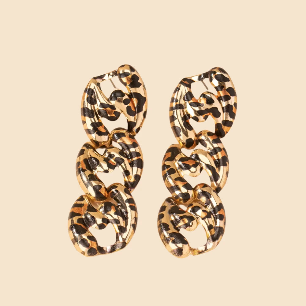 A pair of bold statement earrings featuring a leopard print pattern in black and gold. Each earring consists of three interlocking chain links with a smooth, shiny finish. The earrings are displayed against a light beige background, emphasizing their unique and fashionable design.