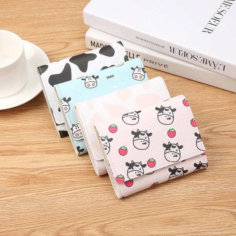 A showcase of four different designs offered. From back to front: black and white cow print, light blue and cow, plain light pink, and light pink with strawberries and cows print sitting on a desk in a line.