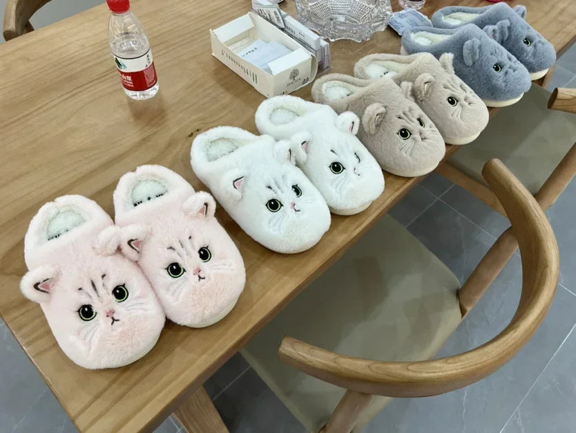 A showcase of the Fuzzy Cat Unisex House Slippers in the colors pink, white, brown, and gray line up on a table. 