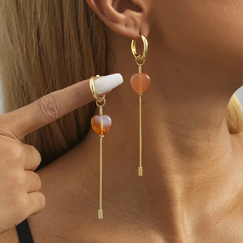 A showcasing of the medium length Heart Chain Geometric Earrings on a female model, one in her ear and one being held up by her finger to give speculation of length.