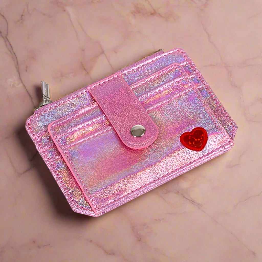 A showcasing of the Pink Glitter Wallet with a little red heart laid flat to show the front of the wallet. 