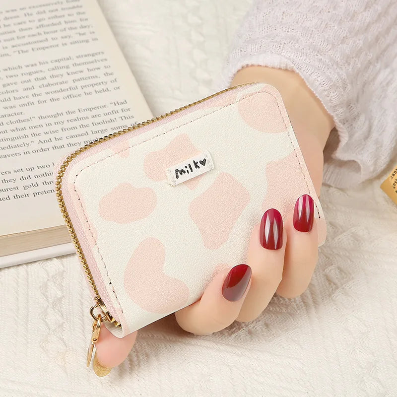 A showcasing of the Pink and White Cow Print Card Bag being held in a hand to show the size comparison. This card bag has a little tag on the front that says milk. 