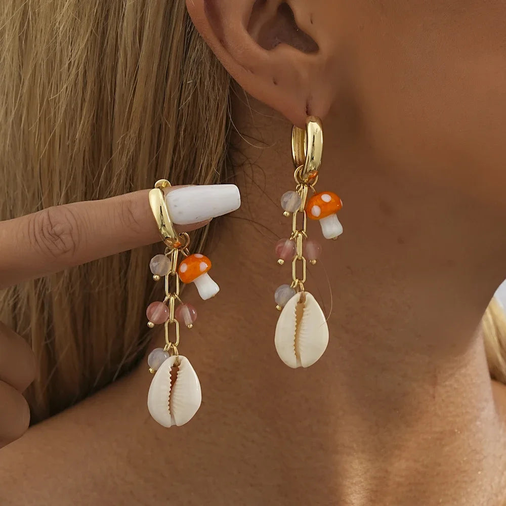 A showcasing of the Short Mushroom and Shell Geometric Earrings on a female model, one in her ear and one being held up by her finger to give speculation of length. 