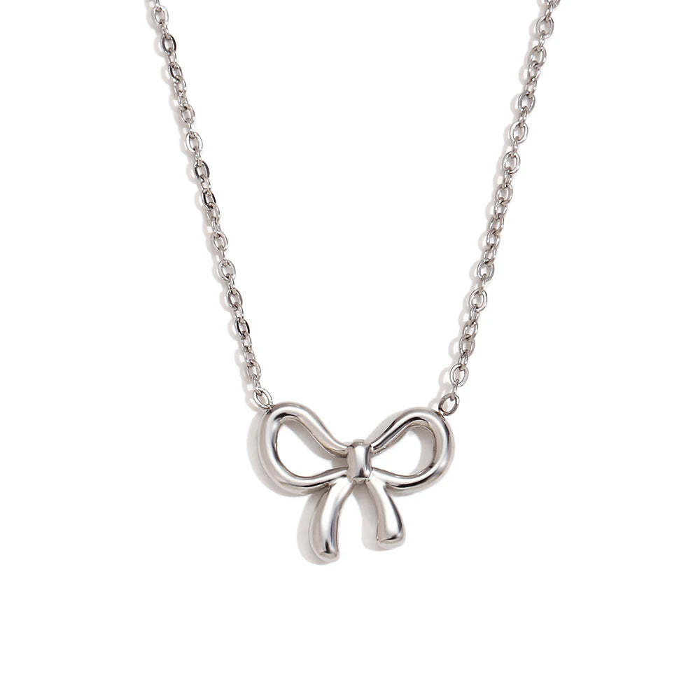 A close-up image of a silver necklace with a Coquette bow-shaped pendant. The chain is made of interlocking oval links, and the pendant is a polished, metallic Coquette bow with smooth, rounded edges. The bow design is simple yet elegant, making it a versatile accessory for various outfits and occasions.