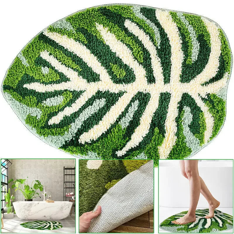 An oval-shaped rug with a white background featuring a detailed tropical monstera leaf pattern in various shades of green. The leaf design includes prominent veins and sections, giving the rug a natural and vibrant appearance.