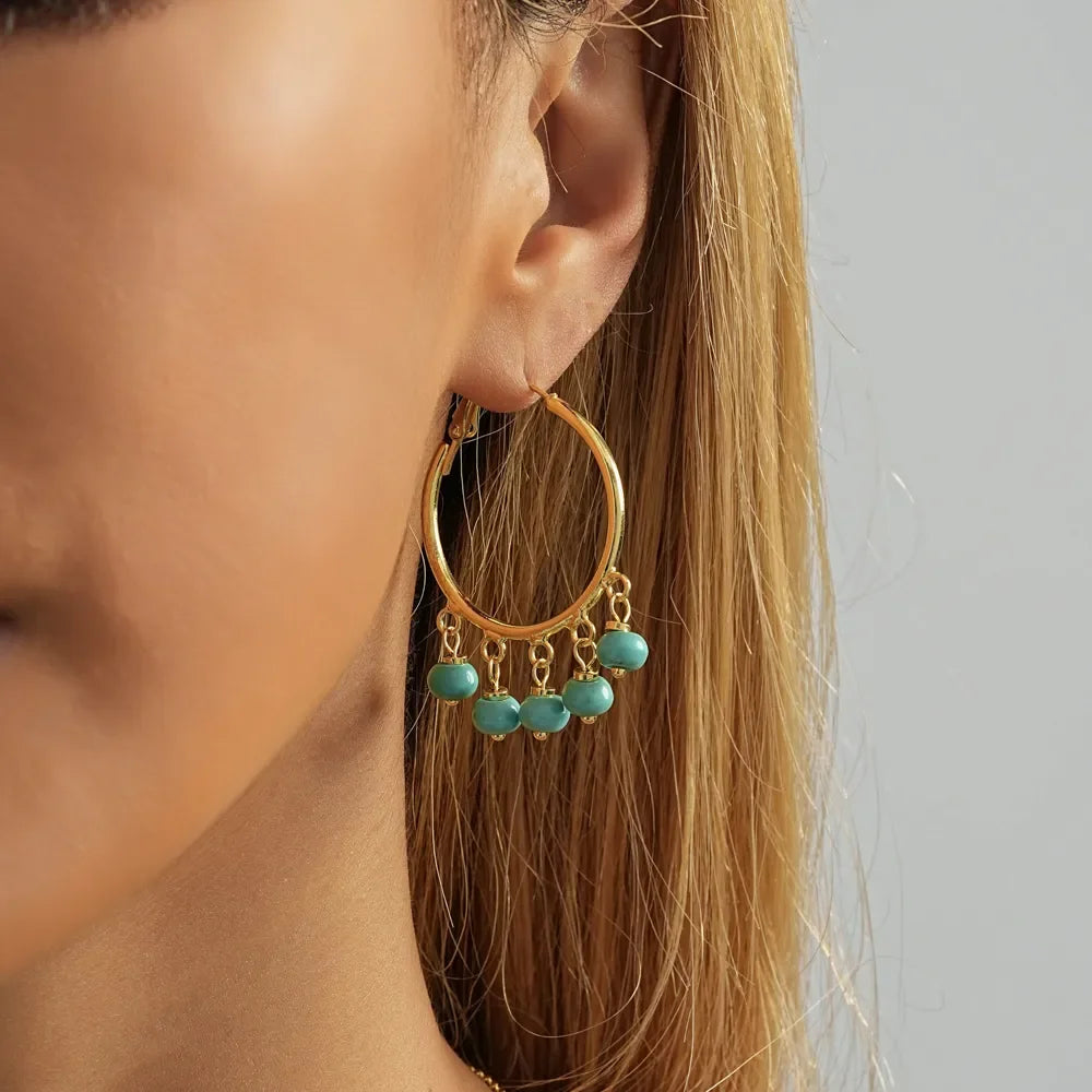 A showcasing of the Turquoise and Gold Hoop Geometric Earrings on a female model in her ear. 